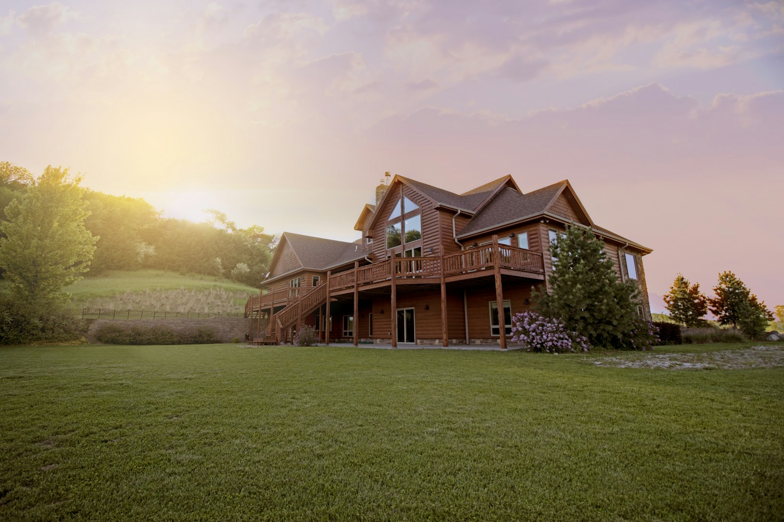 A timber home with a broad porch overlooking a lawn at sunset